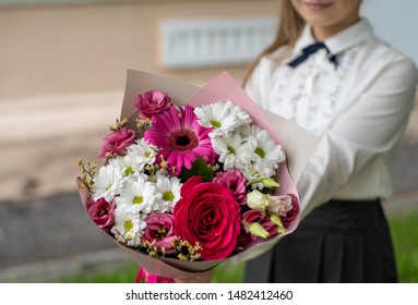 School Girl Dressed In School Uniform Holding A Bright Pink Festive Bouquet Of Beautiful Flowers For Teacher. No Face. Blurred Background.