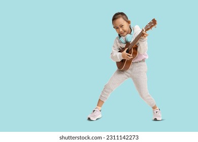 School girl, Happy smiling Asian student school kid hand holding guitar ukulele, Full body portrait isolated on pastel plain light blue background - Powered by Shutterstock