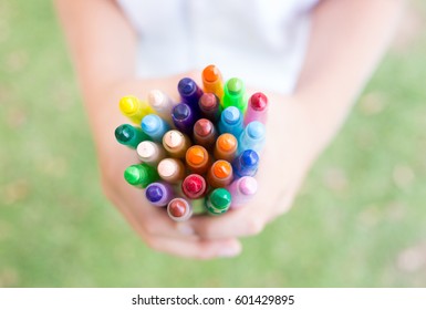 A School Girl Holding Her Colourful Crayons In Her Two Hands.