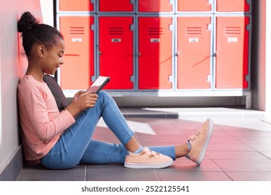 In school, girl sitting on floor using tablet near red lockers. Education, technology, learning, schoolgirl, hallway, digital - Powered by Shutterstock