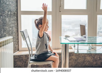 School girl  is studying online. Home schooling. Distance education. The girl raises her hand to answer the teacher's question.