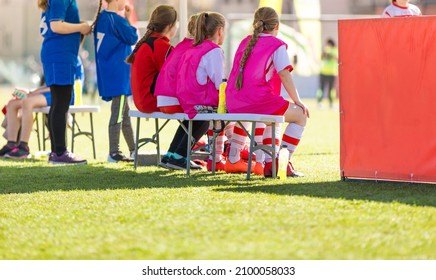 School Girls Sitting On Football Bench And Watching Tournament Game. Female Youth Soccer Team Playing Competition Game On Summer Day. Female Football Tournament