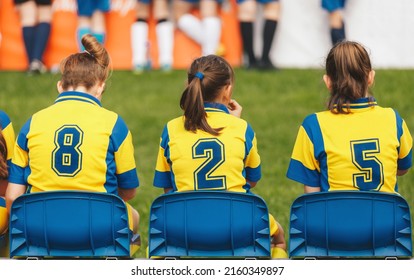 School Girls Sitting On Football Bench And Watching Tournament Game. Female Youth Soccer Team Playing Competition Game On Summer Day. Female Football Tournament