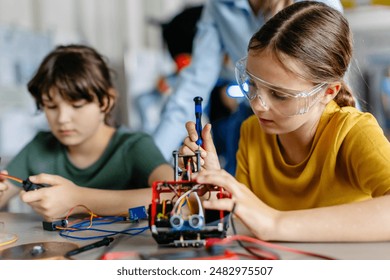 School girls working on circuit board of small robot, building robotic car in after-school robotics club. Children learning robotics in Elementary school. Girls in science. - Powered by Shutterstock