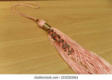 School Graduation Tassel For 2022 Year. Light Pink Tassel With Gold Number Year Charm On Wood Background