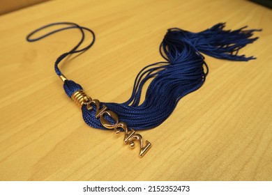 School Graduation Tassel For 2022 Year. Blue Tassel With Gold Year Number Charm On Wood Background.