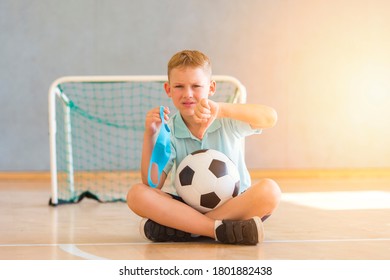 School Kid With Blue Mask And Soccer  Ball In A Physical Education Lesson. Safe Back To School During Pandemic Concept. Social Distancing To Fight COVID-19