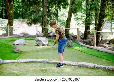 School Kid Boy Playing Mini Golf With Family. Happy Child Having Fun With Outdoor Activity. Summer Sport For Children And Adults, Outdoors. Family Vacations Or Resort.