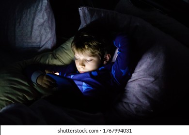 Niño de escuela leyendo un ebook por la noche. Un niño adorable en la cama con un libro interesante.