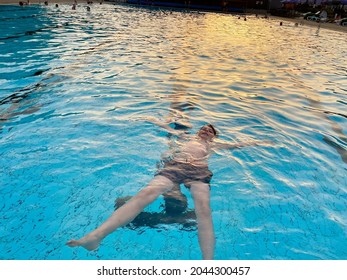 School Kid Boy Splashing In An Outdoor Swimming Pool On Warm Summer Day. Happy Healthy Preteen Child Enjoying Sunny Weather In City Public Pool. Kids Activity Outdoors With Water.