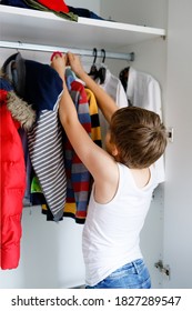 School Kid Boy Standing By Wardrobe With Clothes. Child Making Decision For School Shirt To Wear. Children Get Dressed In The Morning For School.