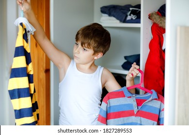 School Kid Boy Standing By Wardrobe With Clothes. Child Making Decision For School Shirt To Wear. Children Get Dressed In The Morning For School.