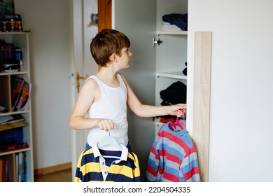 School Kid Boy Standing By Wardrobe With Clothes. Child Making Decision For School Shirt To Wear. Children Get Dressed In The Morning For School.