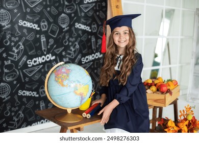 School Kid in graduate headdress is studying in classroom against of blackboard. Smiling little girl in a school uniform and master's hat holding globe in classroom. Back to school, learning lessons.  - Powered by Shutterstock