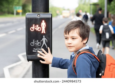 School kid pressing a button at traffic lights on pedestrian crossing on way to school. Child boy with backpack using traffic signal controlled pedestrian facilities for crossing road. - Powered by Shutterstock