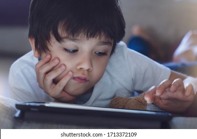 School Kid In Self Isolation Using Tablet For Homework,Child Sad Face Lying Down On Sofa Looking Deep In Thought,Boy Bored Stay At Home During Covid-19 Lock Down,Social Distance Learning Online Educat