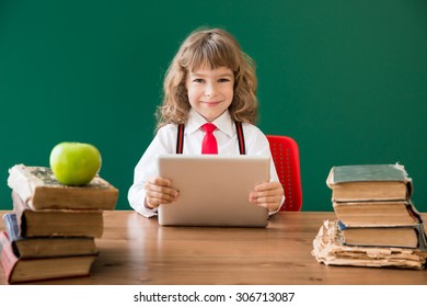 School Kid Sitting At Desk In Class. Happy Child Against Green Blackboard. Education Concept