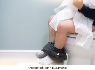 School kid sitting on toilet and playing with toilet rolls, Low view on his legs hanging with grey trousers with fluffy socks,Child tearing the tissue, copy space,Training child or Health care concept