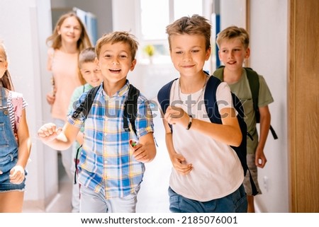 School kids enjoy free time running to camera in elementary school hallway.