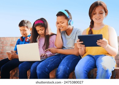 School kids, friends and happy with phone, tablet and laptop with diversity, relax and streaming in summer. Girl, boy and group with headphones, smile and games with subscription on wall at academy - Powered by Shutterstock