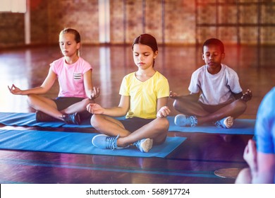 School Kids Meditating During Yoga Class In Basketball Court At School Gym