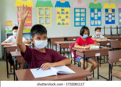 School Kids Wearing Protective Mask To Protect Against Covid-19,Group Of School Kids With Teacher Sitting In Classroom And Raising Hands,Elementary School,Learning And People Concept.