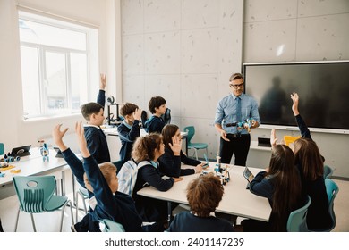 School kids wearing school uniform raising hands to answer question from male school teacher during lesson in stem education class - Powered by Shutterstock