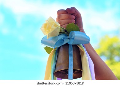 School. The Last Call Or September 1st. Bell In The Hands Of The Child. It Is Decorated With Colored Ribbons Of Pastel Tones And A White Rose. The Concept Of The Beginning Or End Of The School Year.