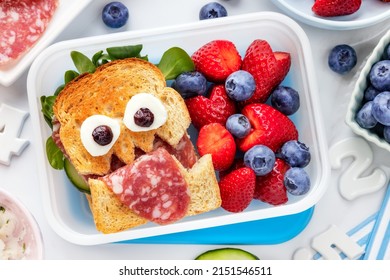 School Lunch Box With A Cute Monster Sandwich With Salami And Fresh Berries Like Strawberries And Blueberries. Overhead View Flat Lay