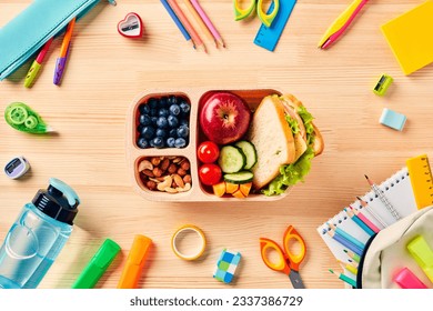 School lunch box with healthy food and school supplies on wooden table. Back to school concept. Top view. Flat lay.