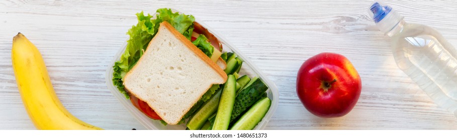 School Lunch Box With Sandwich, Fruits And Bottle Of Water On A White Wooden Surface, Top View. From Above, Overhead. 