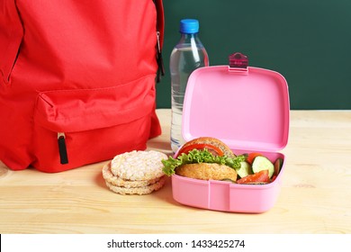 School Lunch Box With Tasty Food And Backpack On Table In Classroom