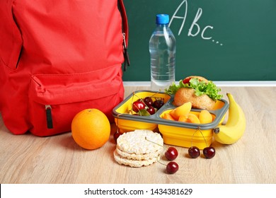 School Lunch Box With Tasty Food And Backpack On Table In Classroom