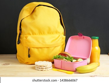 School Lunch Box With Tasty Food And Backpack On Table In Classroom