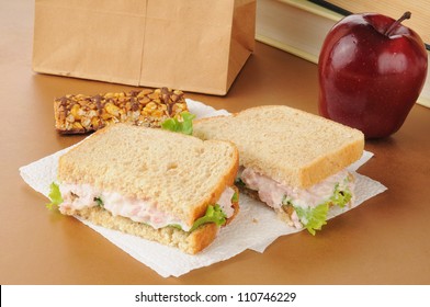 A School Lunch With A Deviled Ham Sandwich, Apple, Granola Bar And Textbooks