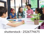 In school, middle-aged African American teacher laughing with diverse students. They are gathered around table with sustainability poster behind them, learning, education, unaltered