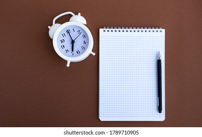 School Notebook Pen And White Alarm Clock On A Brown Background. Back To School. Flatlay. Copy Space