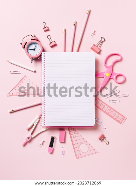 School and office pink equipment with empty\
notebook with copy space on pastel pink background. Accessories\
with retro alarm clock. Creative back to school concept. Flat lay,\
top view.