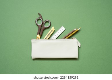 School office writing supplies in pencil case on green desk. top view, copy space Foto Stock