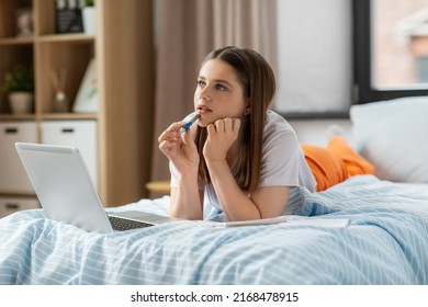 school, online education and e-learning concept - thinking or daydreaming teenage student girl with laptop computer writing to notebook lying on bed at home