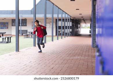 In school, outdoors, young biracial male student wearing a red backpack is running with copy space. He has short dark hair, light brown skin, and is wearing casual clothes, unaltered. - Powered by Shutterstock