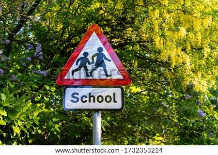 school sign in London, UK.  Warning to slow down road sign with trees in the background