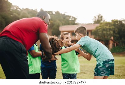 School sports team having a huddle in a rugby field. Trainer giving his students a motivational pep talk before practice. Sports coach mentoring children in elementary school. - Powered by Shutterstock