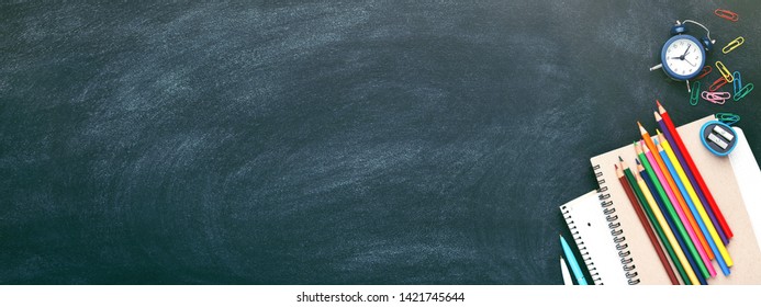 School stationary on blackboard. Notebooks, pens, pencils, alarm clock, red apple and other tools. Banner with place for text. - Powered by Shutterstock