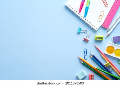 School stationery, color pencils, paints, notepad on blue table. Back to school background. Kids desk top view.