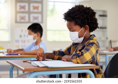 School Student In Class During Covid Pandemic For Learning, Education And Study With Mask For Safety, Protection And Protocol. Little Kindergarten, Preschool Or Elementary Kid Writing In Book At