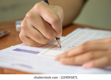 School Students Hands Taking Exams, Writing Examination Holding Pencil On Optical Form Of Standardized Test With Answers Sheet Doing Final Exam In Classroom. Education Assessment Concept. Soft Focus