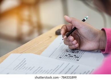 School Students hands taking exams, writing examination room with holding pencil on optical form of standardized test with answers and english paper sheet on desk doing final exam in classroom.