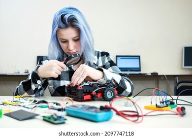 School students making robotic cars. Teenager girl at robotics school makes robot managed from the constructor, child learns robot constructing.