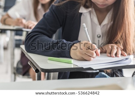 School student's taking exam writing answer in classroom for education and literacy concept